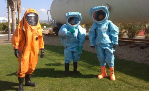 Three people in hazmat suits outdoors.